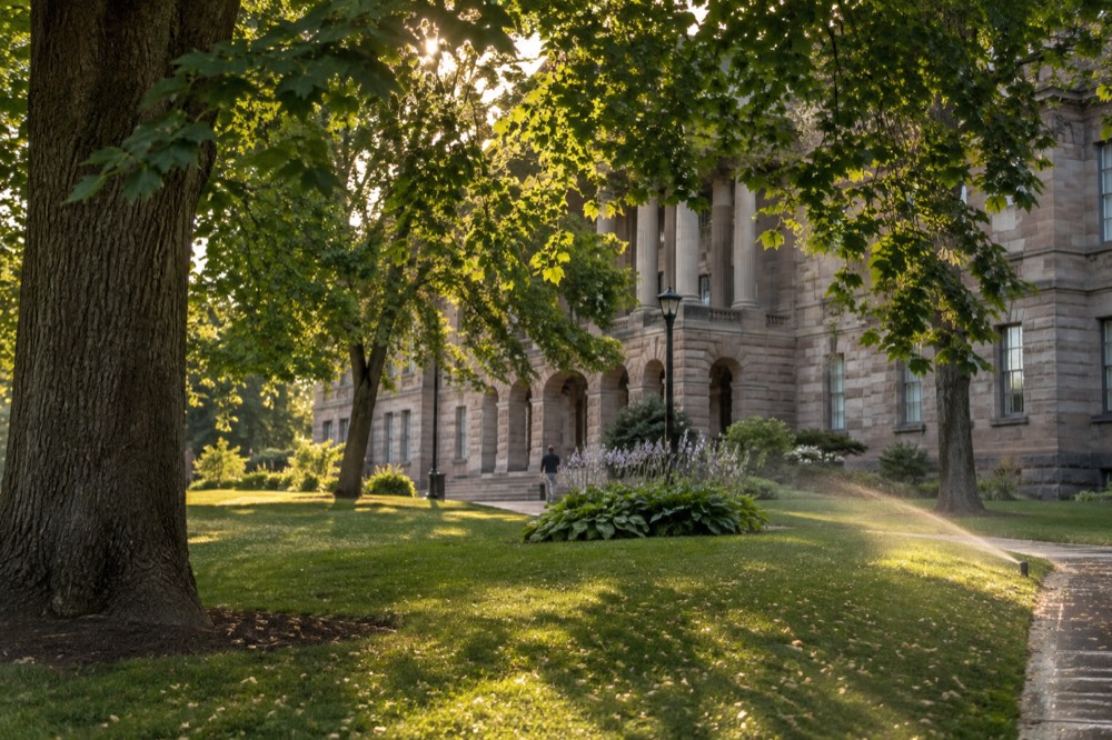 A quiet park bench under mature trees beside a historic stone building