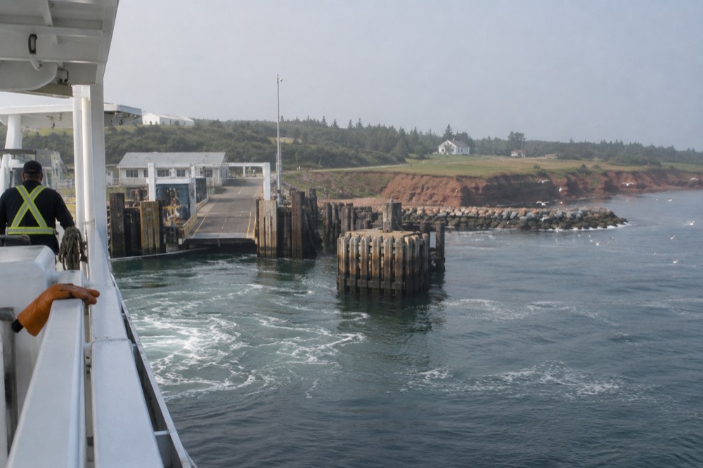 A white ferry approaching a small island wharf across calm blue water