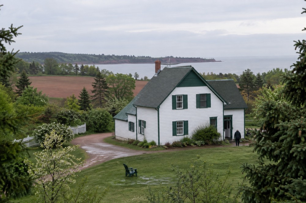 A white farmhouse with green gables surrounded by trees and farmland