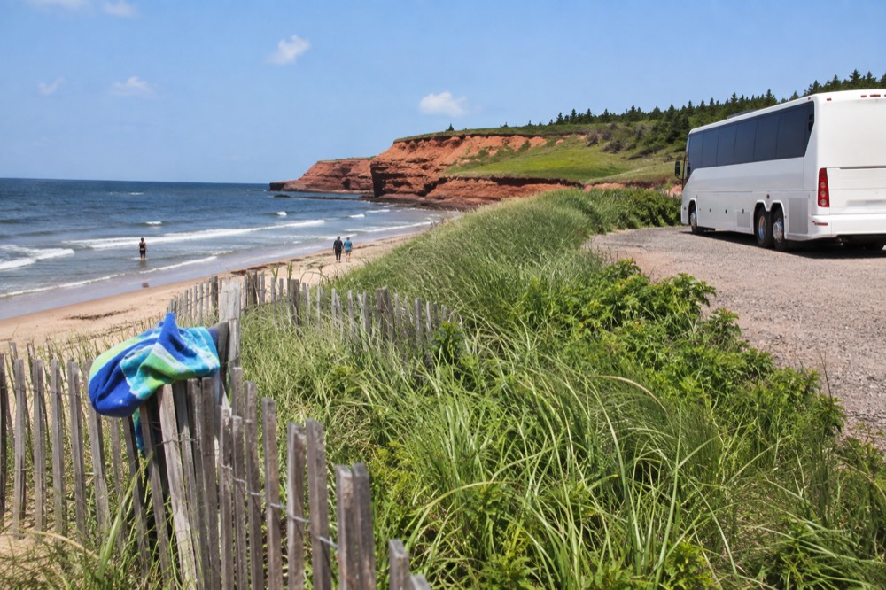 A tour bus parked beside red cliffs overlooking a sandy beach
