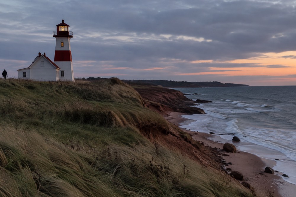 A red lighthouse on a point of dune grass above the sea at dusk