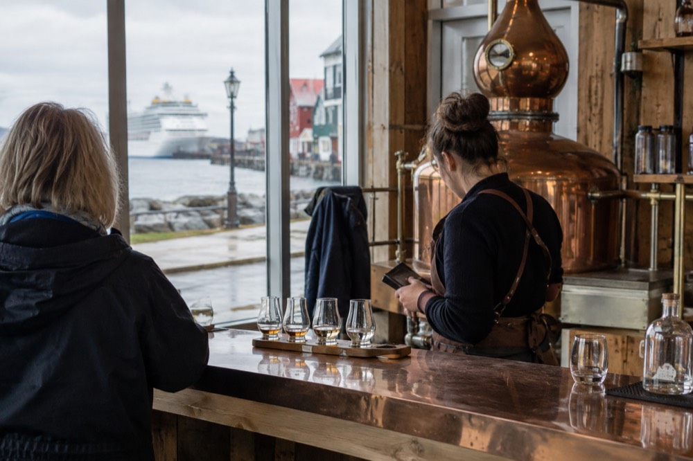 A distillery tasting counter with small sample glasses and a barkeeper checking identification