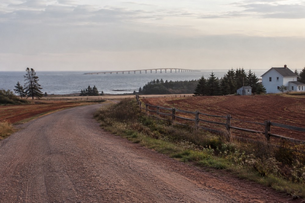 Country road curving past red farm fields toward the sea